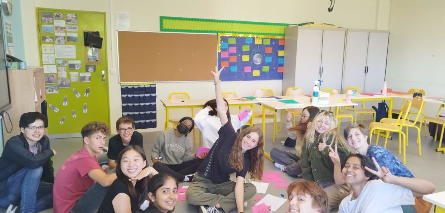 Students sitting in a circle, posing for the camera with red revision game cards on the floor