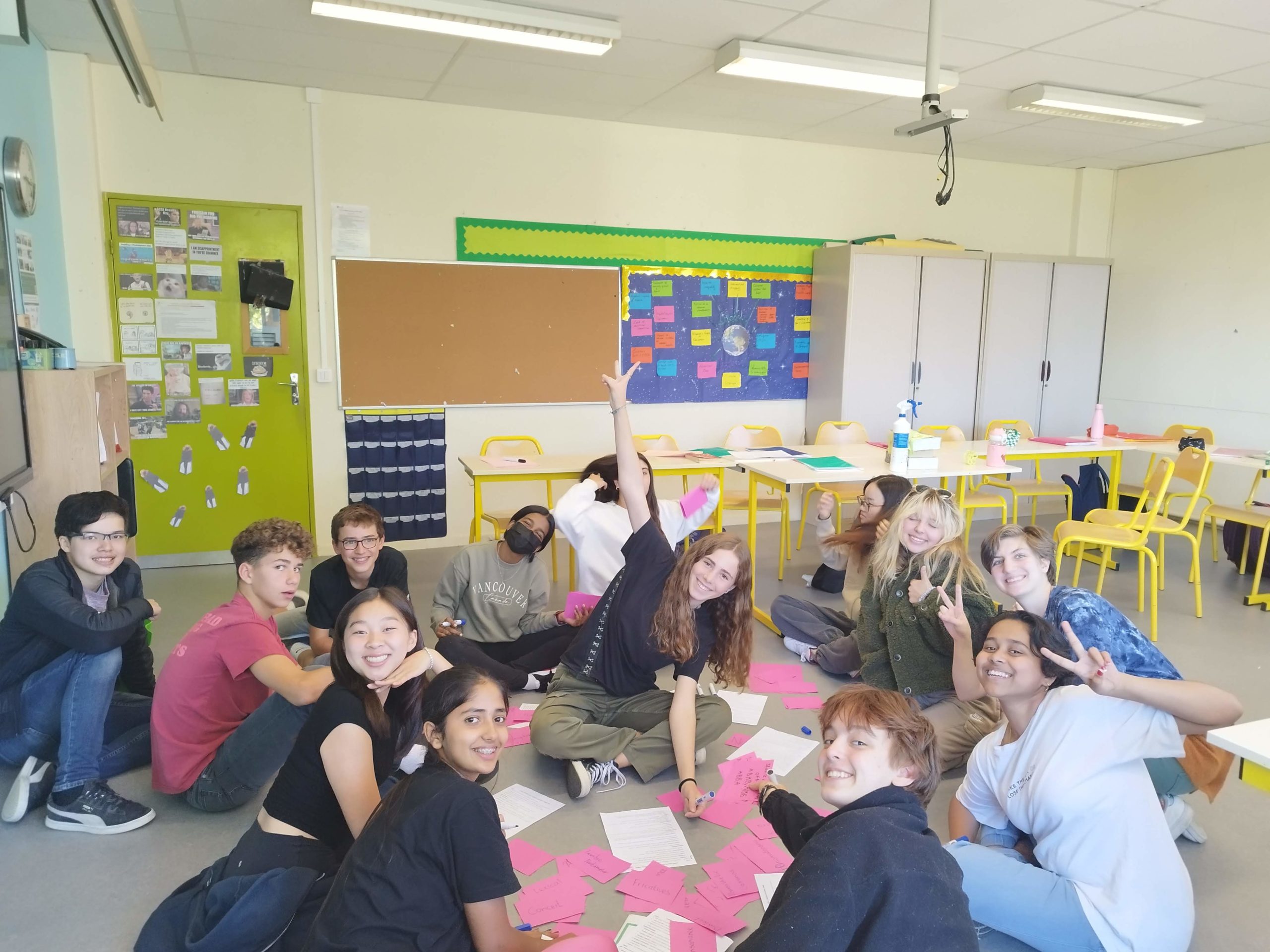 Students sitting in a circle, posing for the camera with red revision game cards on the floor