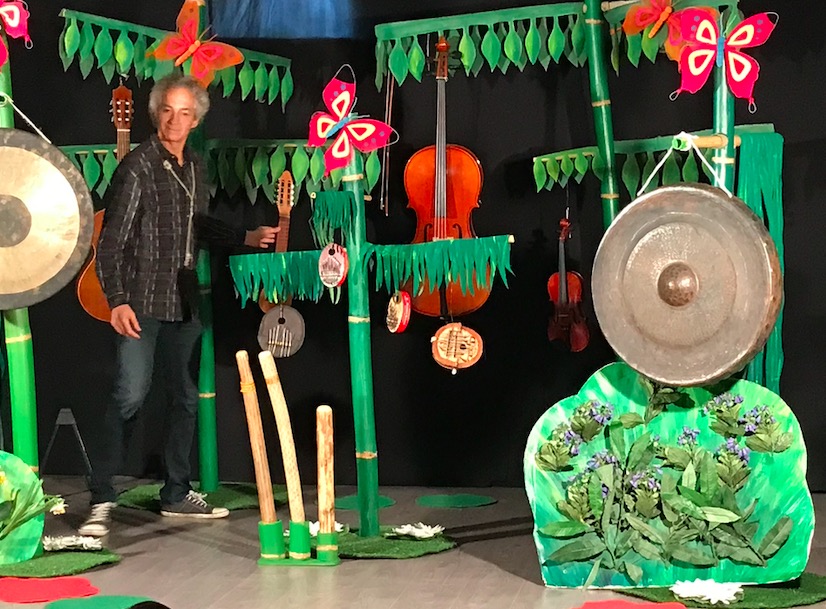 Luc standing in front of a jungle-themed background with various instruments hanging from the foliage