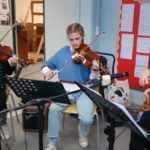 2 students and a teacher playing violins