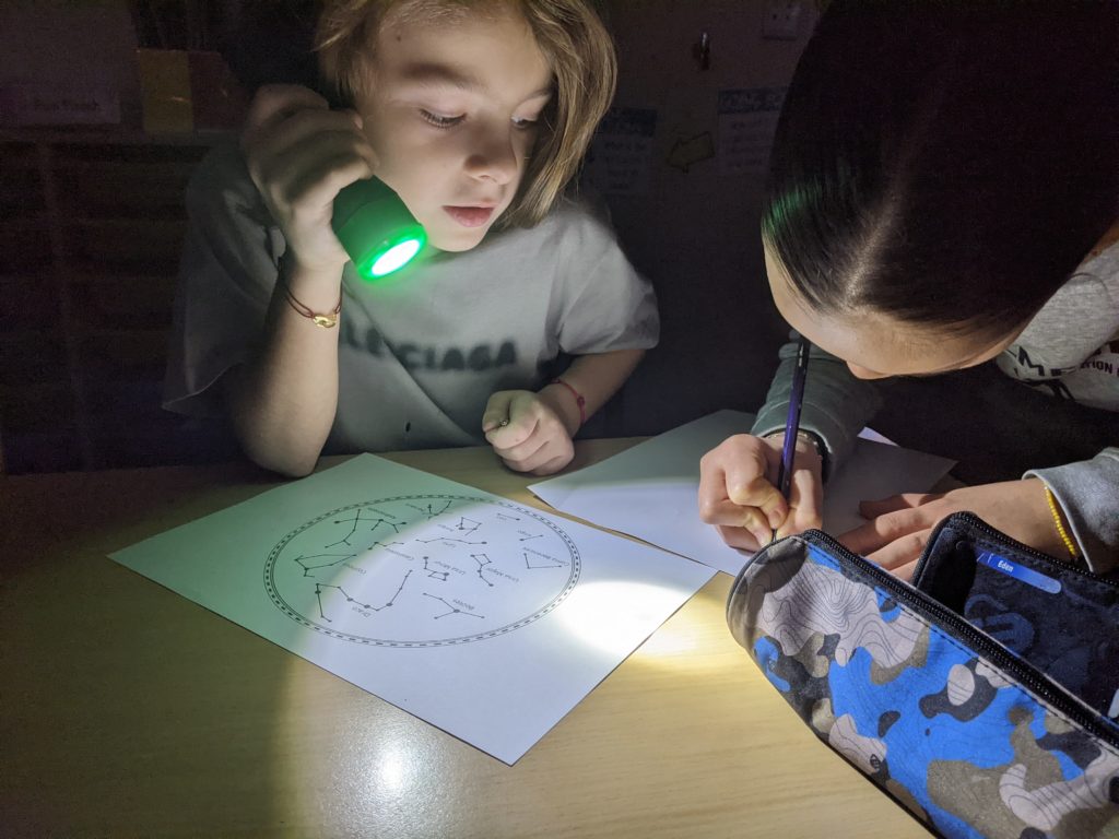 Student holding a flashlight while another student draws constellations