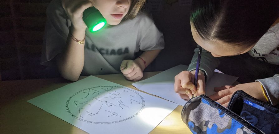 Student holding a flashlight while another student draws constellations