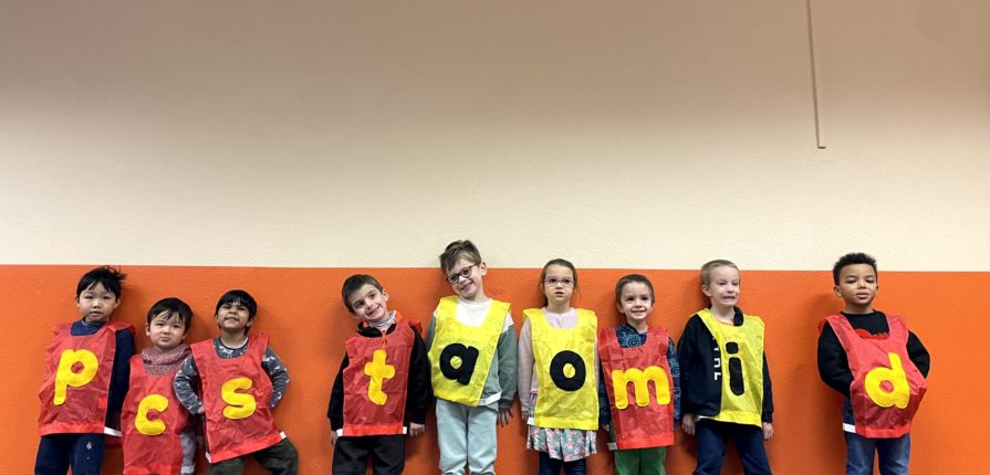 Kindergarten students lining up while wearing bibs with different letters on them