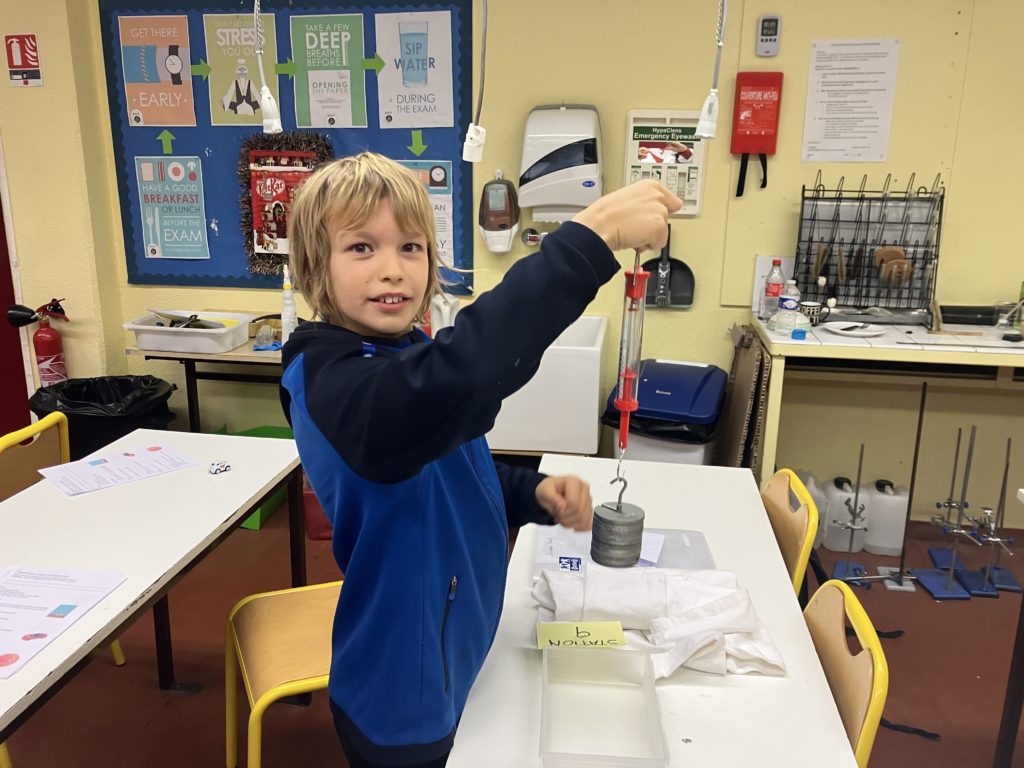 A middle school student holding a force meter with suspended masses
