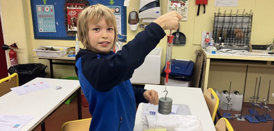 A middle school student holding a force meter with suspended masses