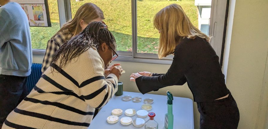 A student showing a petri dish to a teacher and another student