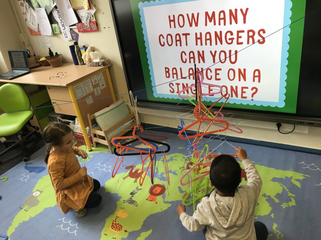 2 students trying to balance as many coat hangers as possible on a single hanger