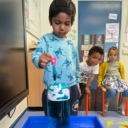 Kindergarten students using an eye dropper to add blue water to a cylinder to demonstrate how rain works