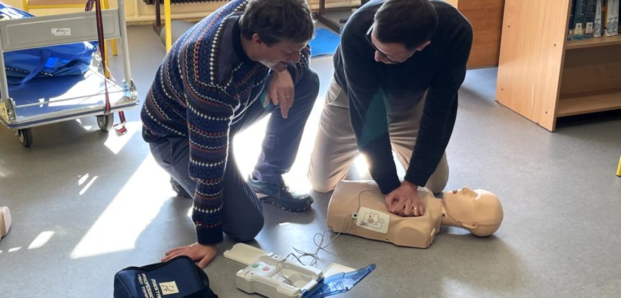 2 staff members practicing CPR and using a defibrillator with a training dummy