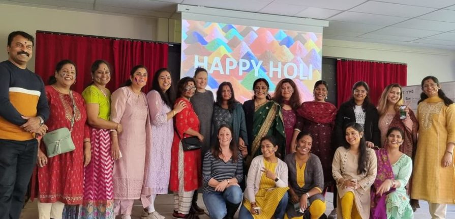 Parents posing in front of a sign that reads "Happy Holi"