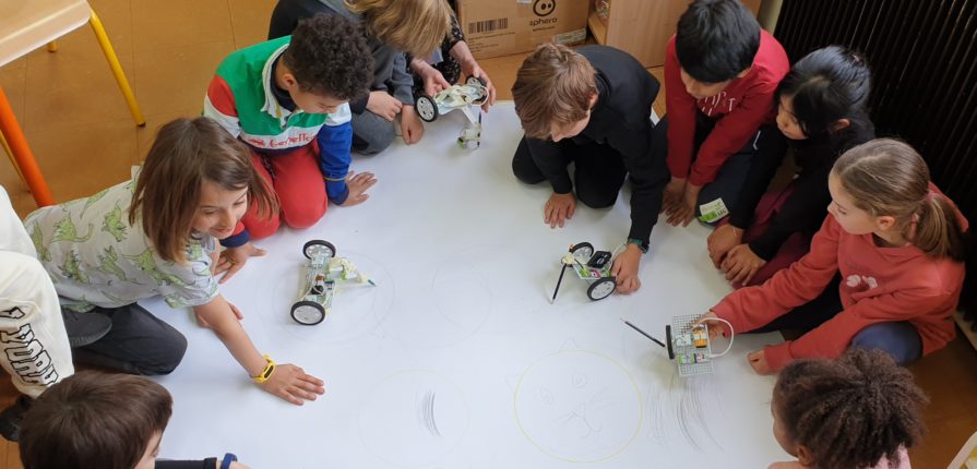 Students sitting on a large piece of paper, testing out their art robots.