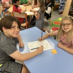2 students sitting at a table in the library, working on a buddy activity