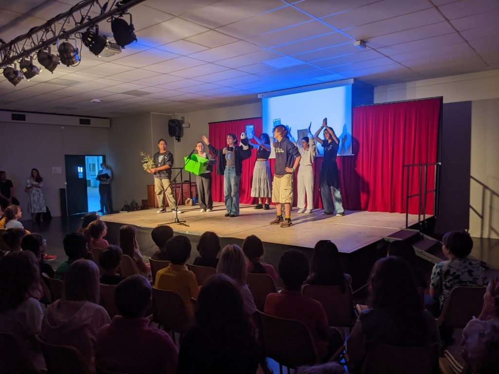 Secondary students standing on a stage, delivering a presentation about reducing waste using a projector