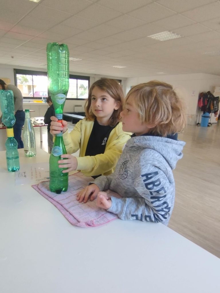 2 boys holding water bottles connected together, demonstrating how a vortex works