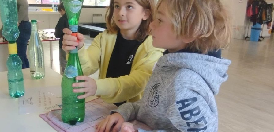 2 boys holding water bottles connected together, demonstrating how a vortex works