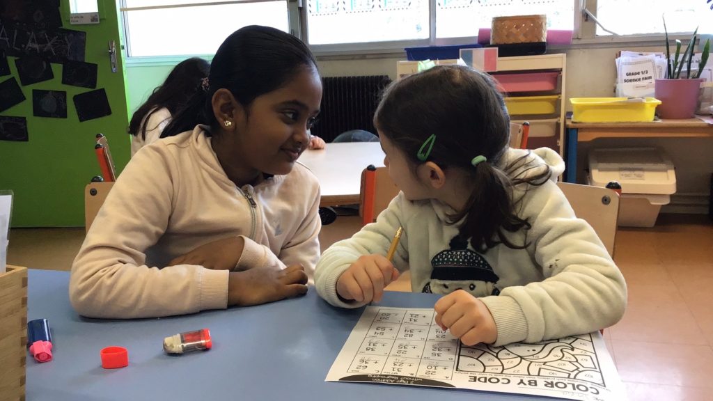 2 students looking at each other while completing a math worksheet