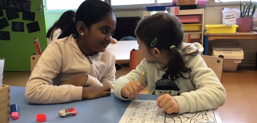 2 students looking at each other while completing a math worksheet