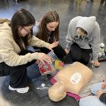 Students applying defibrillator pads to a first aid dummy