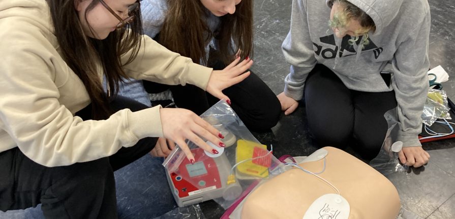 Students applying defibrillator pads to a first aid dummy