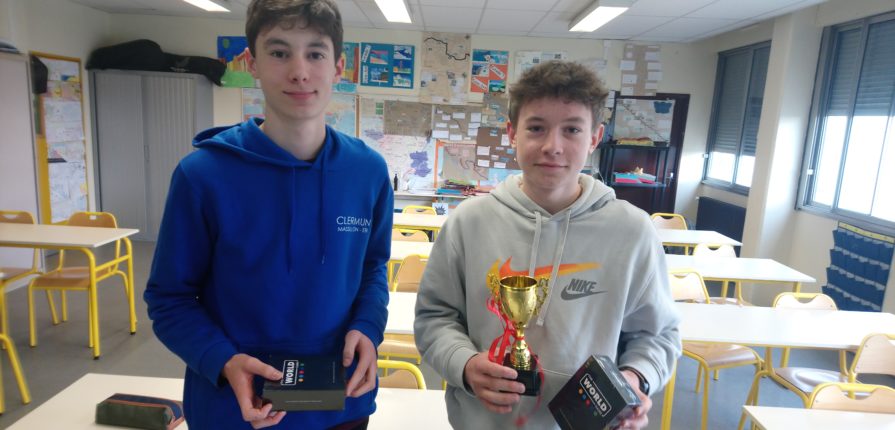 2 students, 1 holding a trophy and both holding other prizes.