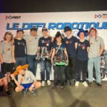 Students posing with their robot in front of a sign reading "Le Defi Robotique"