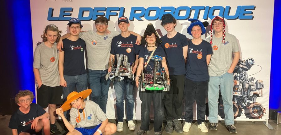 Students posing with their robot in front of a sign reading "Le Defi Robotique"