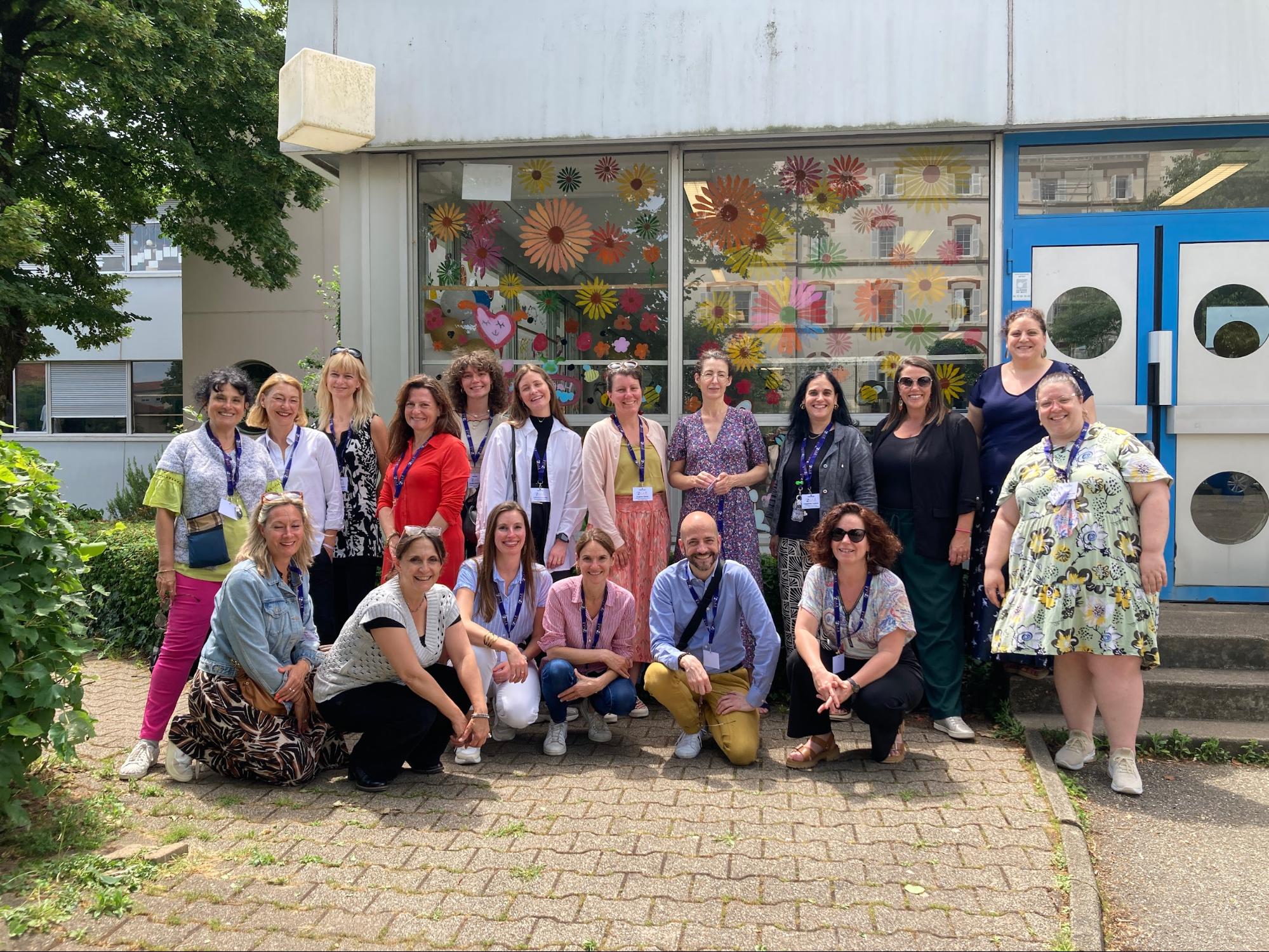 Group photo of French teachers from ISL and visiting international schools, smiling outside ISL with colourful floral window decorations.