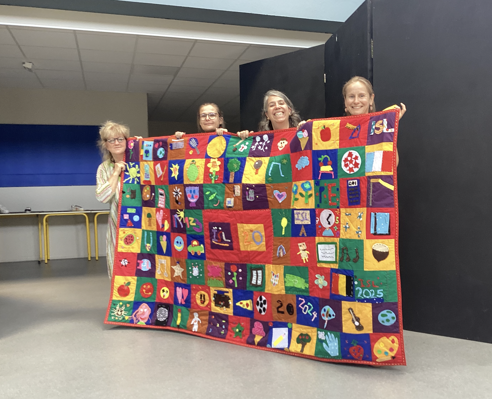 4 teachers holding a colorful quilt created by students for ISL’s 20th anniversary